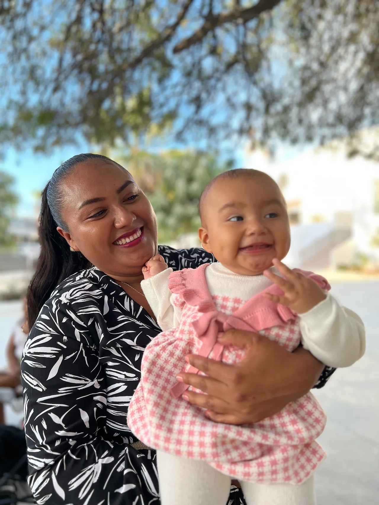 A woman holds a laughing baby girl outdoors