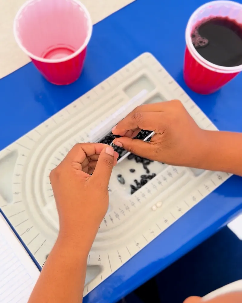Hands thread black beads on a bead board, next to two red cups