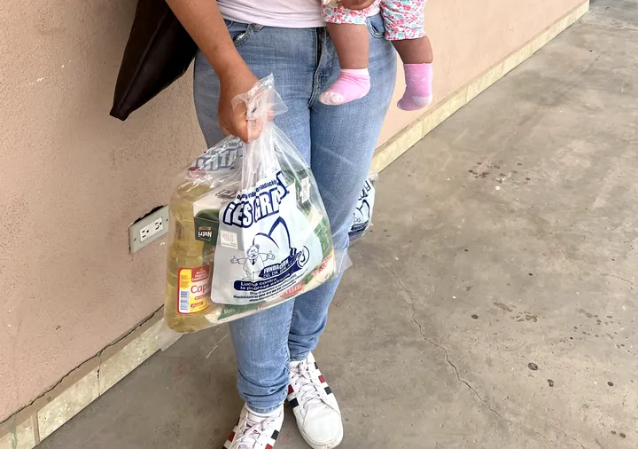 A mom carries her baby and a bag of groceries at VIFAC Los Cabos