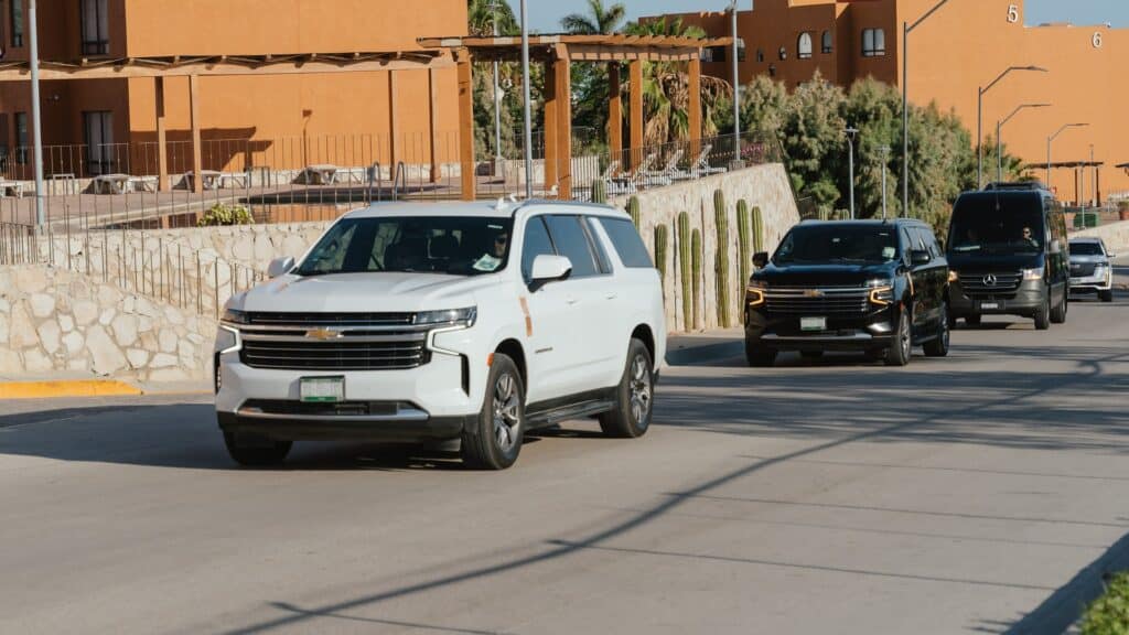 A white Browns Private Services Suburban on the road with a black Suburban and a black Mercedes Sprinter behind
