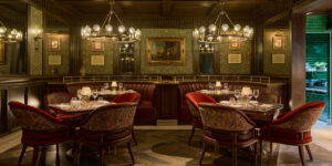 Ornate green-wallpapered dining room with oil painting, sconces and curved leather booth