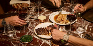 Wood-grilled steak and fish mains shared on a red marble table with red wine