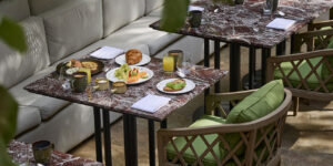 Sunlit courtyard breakfast on marble-top tables with green cushioned chairs and palms