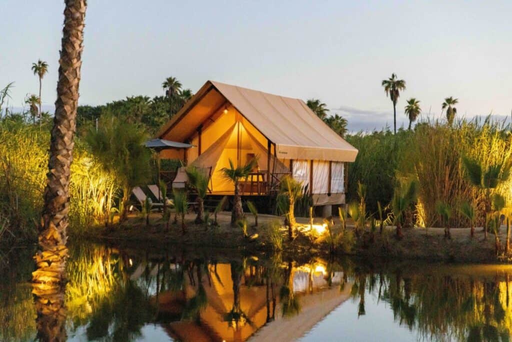 Amet Nature Retreat — a canvas tent on stilts lit at dusk and reflected in a still pond