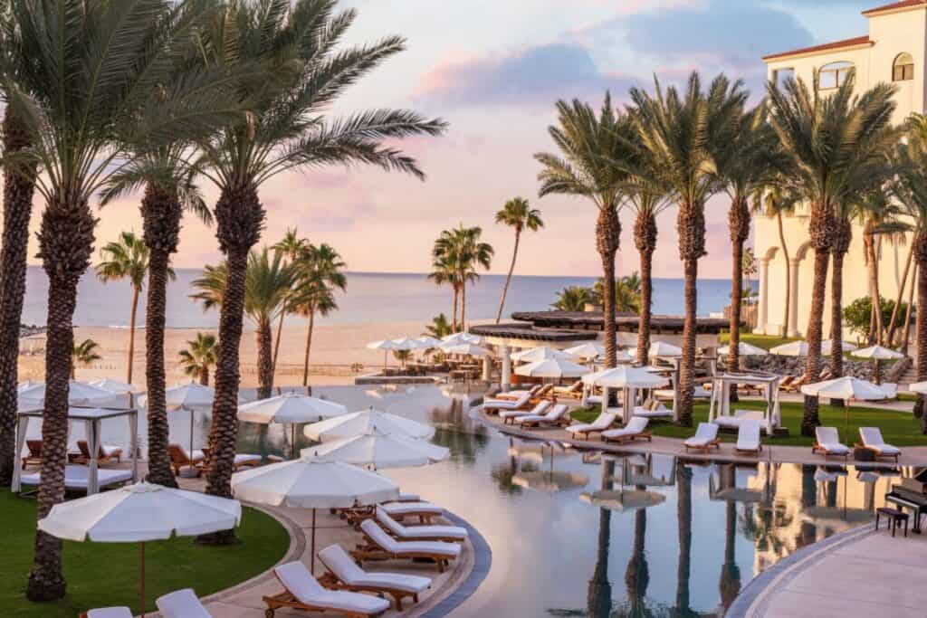 Hilton Los Cabos Beach & Golf Resort — pool framed by palms with white cabanas and loungers at sunset