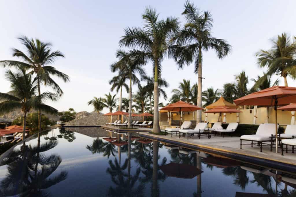 Hacienda Beach Club and Residences — infinity pool reflecting the palms, with loungers and red parasols