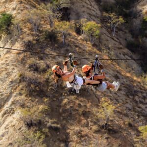 Two riders ziplining side by side across the Wild Canyon in Los Cabos