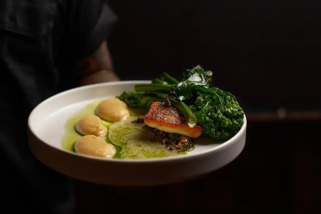 Pan-seared fish fillet with broccolini and green sauce plated at Bar Esquina, Cabo San Lucas