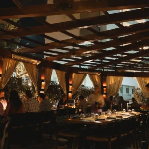 Evening dining room under a wood pergola with curtains and set tables at Bar Esquina, Cabo San Lucas