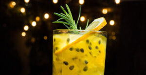 Passionfruit cocktail with rosemary garnish against string lights