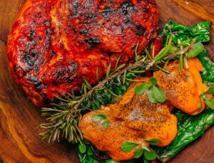 Live-fire grilled meat plated with fresh herbs, greens and roasted chiles