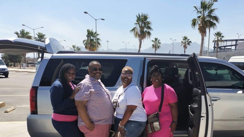 Four travelers beside a silver DanysCabo Chevrolet Suburban with its doors open in the SJD airport parking lot