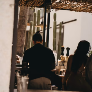 Guests at the palapa-shaded outdoor bar with tall cacti in warm sunlight