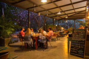 Evening dining in the palapa with pendant lighting, guests at tables and the hand-lettered chalkboard menu