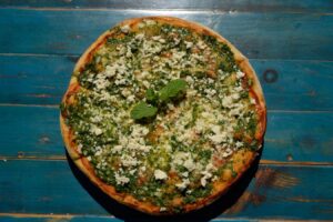 Wood-oven pizza topped with herbs, pesto and crumbled cheese on a blue rustic wooden table