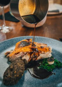Roast suckling pig plated with dark jus poured tableside from a copper pot