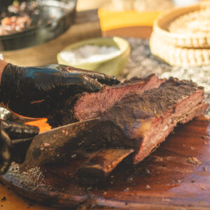 Fire-grilled beef being sliced on a wooden board with salt and garnishes