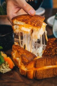 Grilled cheese sandwich with melting cheese pull and pickled vegetables on a wooden board