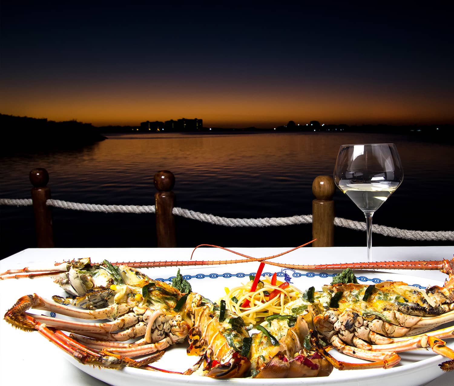 Signature grilled lobster platter with white wine on the marina terrace at sunset at Lorenzillo's