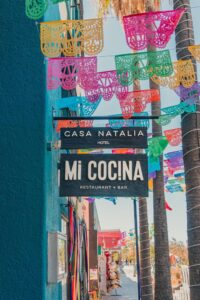 Exterior signage reading Casa Natalia / Mi Cocina Restaurant + Bar with papel picado and palms