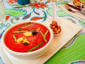 Chilled tomato gazpacho topped with basil and croutons on a colorful table runner