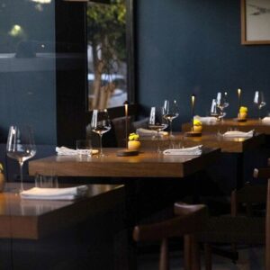 Dining room with set tables, wine glasses and lemon-yellow table candles against a deep blue wall (Michelin Guide photo)