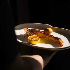 Grilled whole prawn with charred citrus on a ceramic plate held in hand (Michelin Guide photo)