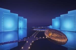 Dusk exterior of the illuminated NIDO nest-dome over the water between the blue-lit towers at Viceroy Los Cabos