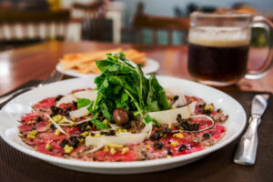 Beef carpaccio with arugula and shaved cheese, plated tableside