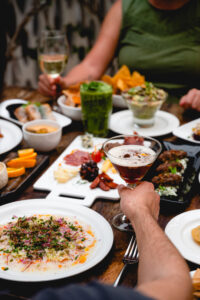 Table spread with shared plates, drinks and a cocktail toast