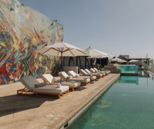 Rooftop infinity pool with striped daybeds, shade umbrellas and the signature mosaic mural wall
