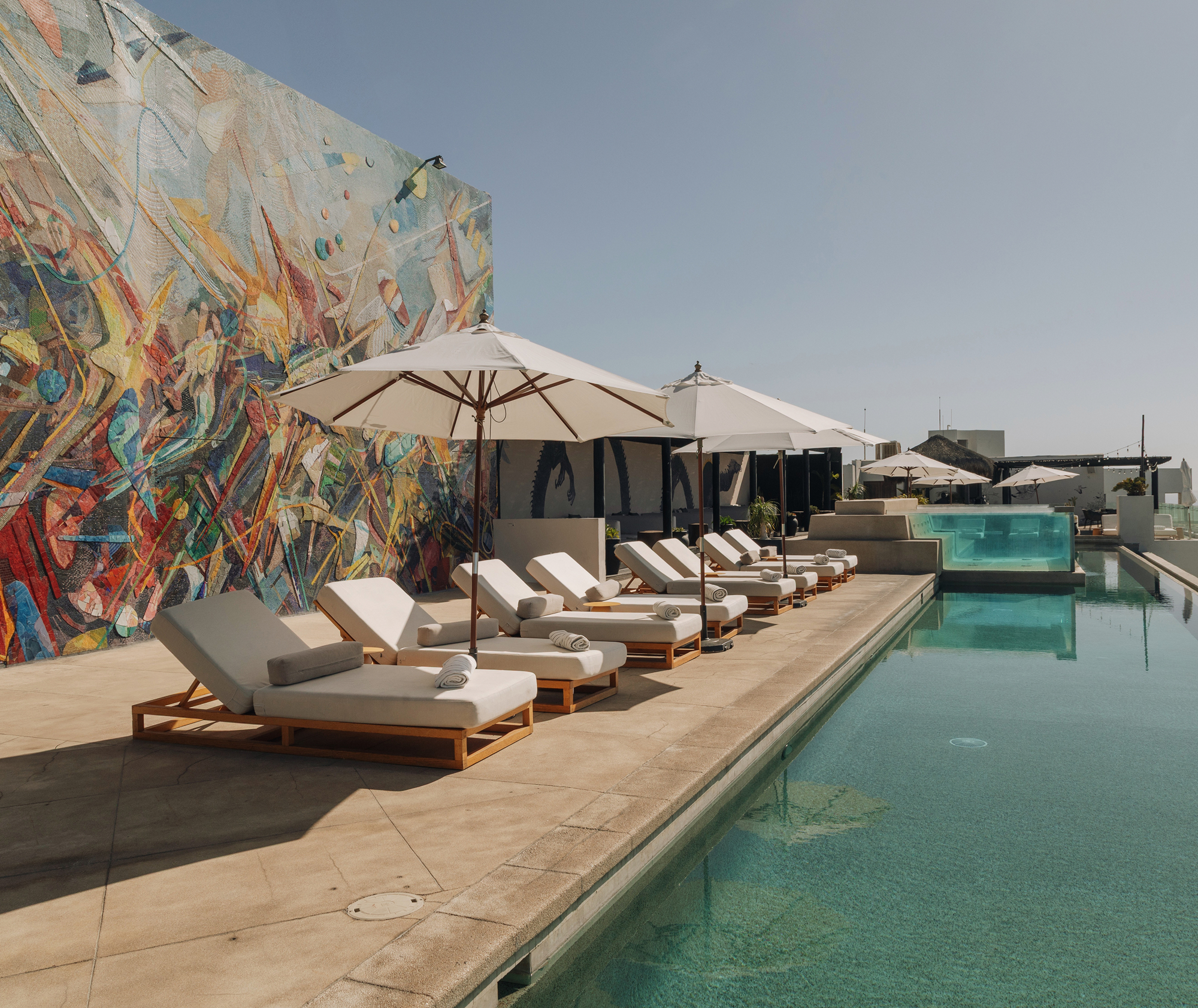Rooftop infinity pool with striped daybeds, shade umbrellas and the signature mosaic mural wall