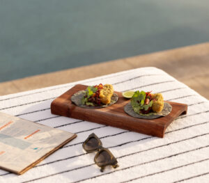 Amaranth tempura tacos on a wood serving board beside the rooftop menu and sunglasses