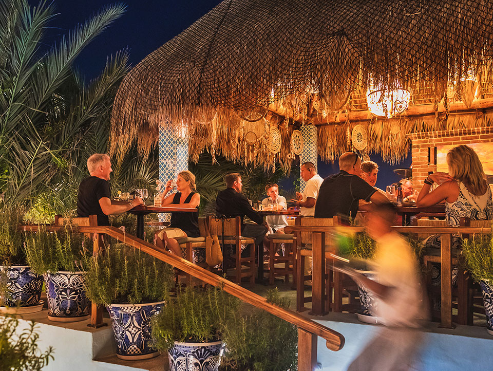 Diners at palapa-roofed terrace tables at dusk at Tres Sirenas, Cabo San Lucas
