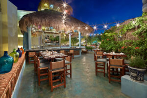 Outdoor patio dining tables under a palapa with string lights at Tres Sirenas, Cabo San Lucas