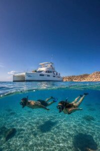 Cabo Adventures power catamaran above two guests snorkeling in a protected bay