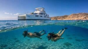 Snorkelers exploring clear water beside a double-deck catamaran in Cabo