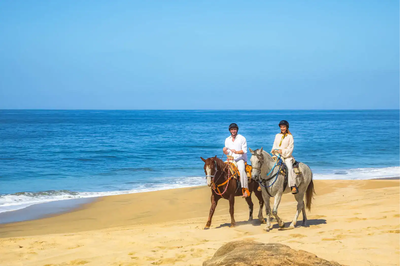 Two riders on horseback beside the Pacific Ocean in Migriño