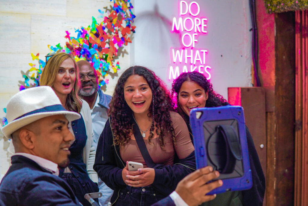 Visitors laughing beside a neon sign and a butterfly wall installation inside a San José del Cabo gallery