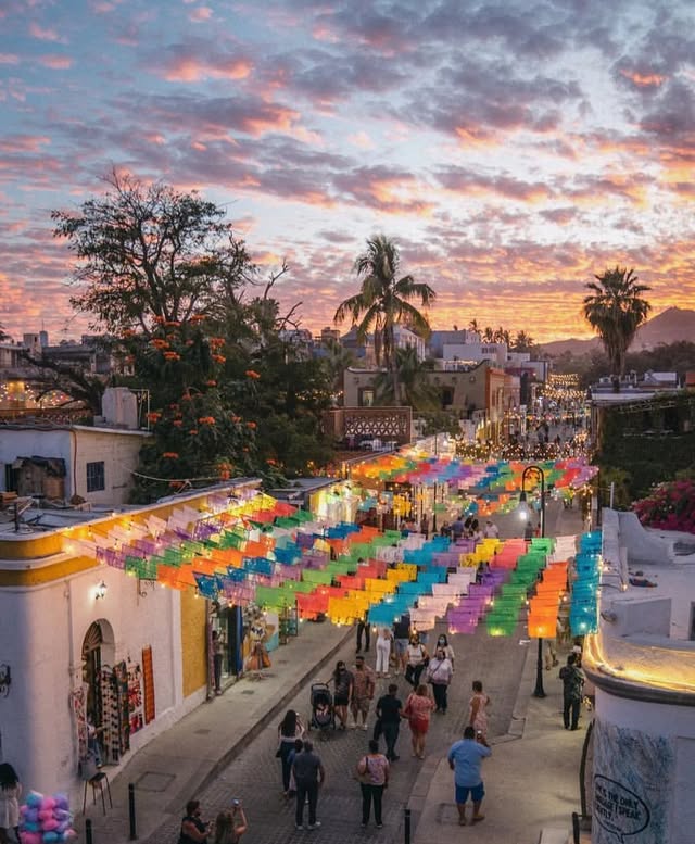 Papel picado strung over the Art District street in San José del Cabo at sunset, with people walking below