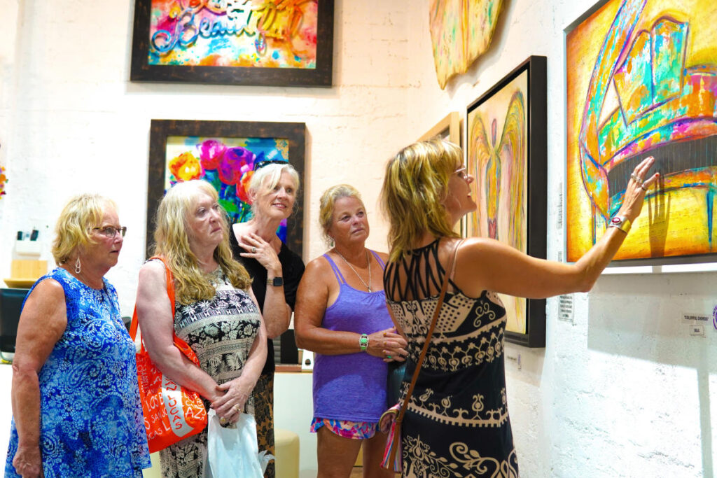 Group looking at colorful paintings on a white gallery wall during the San José del Cabo Art Walk