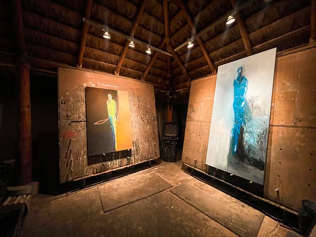 Two large figurative paintings lit inside a timber-roofed San José del Cabo gallery