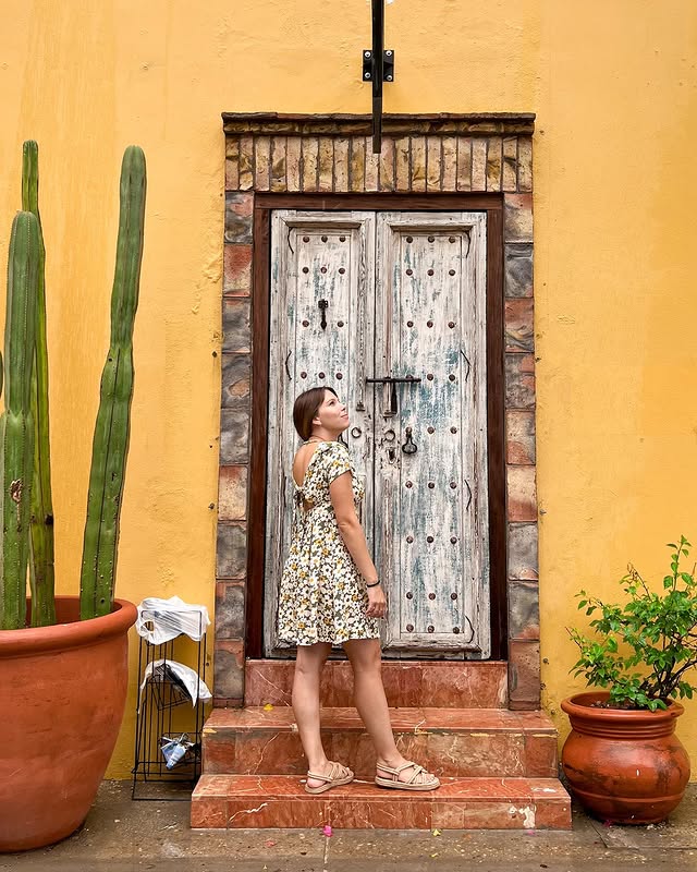Visitor beside a weathered wooden door set into a yellow wall with cacti in San José del Cabo