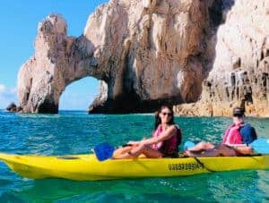 Two guests in a yellow tandem kayak in front of the Arch of Cabo San Lucas