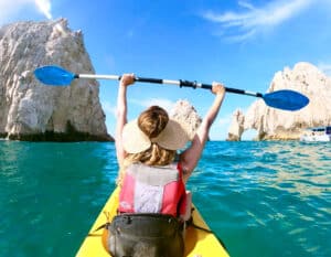 Guest raising a paddle while kayaking toward the Arch in Cabo San Lucas