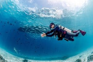 Scuba diver swimming alongside a school of fish in clear blue water