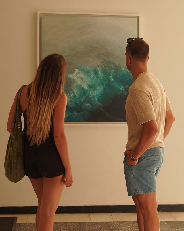 Two visitors standing in front of a large wave painting in a San José del Cabo gallery
