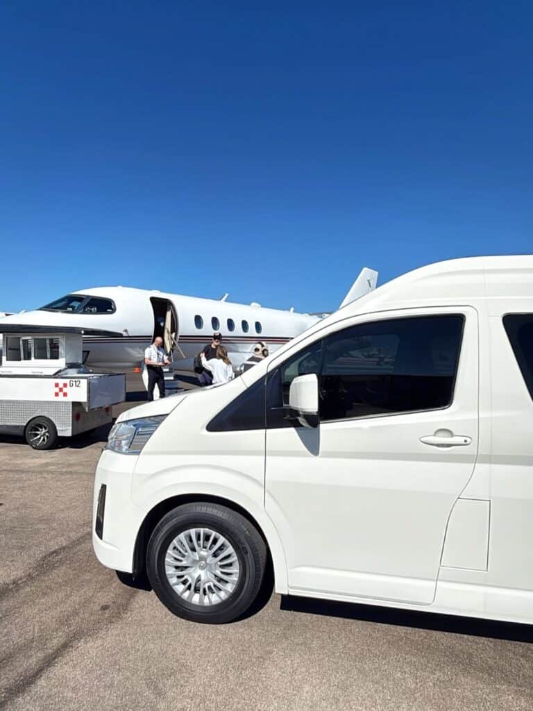 A white passenger van waiting beside a private jet on the Los Cabos apron.