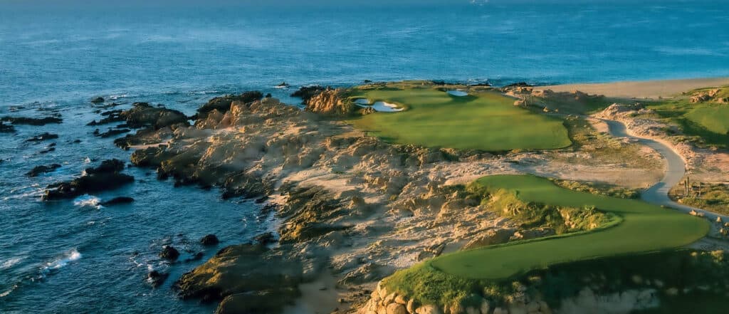 Oceanfront greens at Cove Club above black volcanic rock and turquoise water on the Los Cabos coast