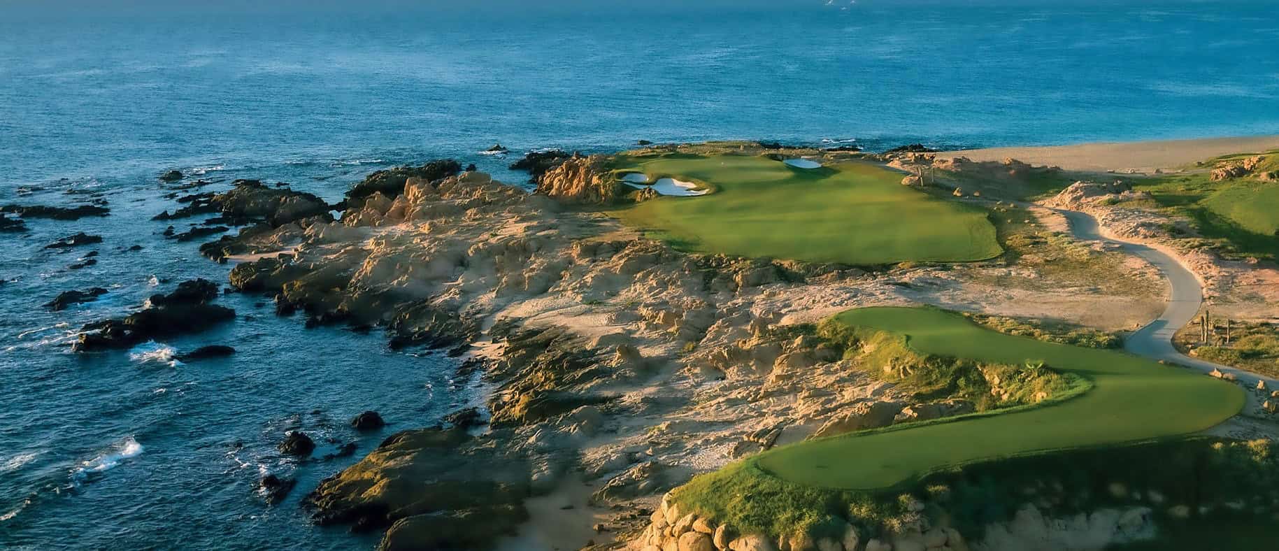 Oceanfront greens at Cove Club above black volcanic rock and turquoise water on the Los Cabos coast